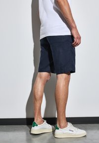 Námořnické šortky vyrobené z texturované látky, nad kolena, spárované s bílými teniskami se zelenými akcenty.