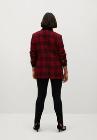Rot und schwarz kariertes Blazer mit langen Ärmeln, Knopfakzenten, kombiniert mit schwarzen Leggings und offenen Schuhen mit Absatz. Glatte Textur, taillierte Passform.