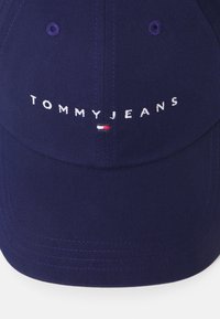 Căciulă marină cu bor curbat. Prezintă text brodat alb "TOMMYJEANS" și un mic logo roșu, alb și albastru. Design structurat cu material texturat.