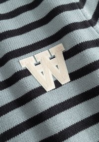 Tissu tricoté rayé bleu et noir avec un emblème texturé blanc en forme de "W" cousu près du centre.