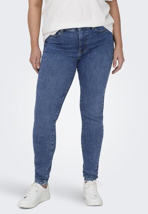 Jeans ajustados de mezclilla azul con una textura suave, cinco bolsillos, pasadores para cinturón y una cintura de altura media, combinados con zapatillas blancas.