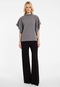 Grijze textuur top met vlindermouwen, hoge hals en subtiel streepjespatroon, gecombineerd met zwarte wijde broek.