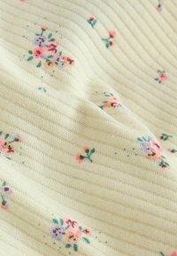 Tissu côtelé crème avec de petits groupes de motifs floraux roses, violets et bruns dispersés à travers la surface.