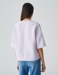 Maglione textured lilla con maniche corte e dettaglio di cucitura sul retro, abbinato a jeans blu. Design semplice e dal taglio comodo.