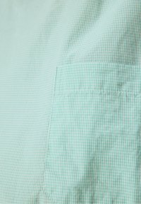 Gros plan d’un tissu à petits carreaux vert clair et blanc avec une poche cousue visible sur le côté droit.