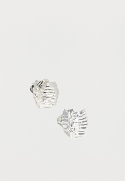 Ασημένια μεταλλικά σκουλαρίκια με ρίγες, ανάγλυφη υφή και κλιπ με μεντεσέ, σε λευκό φόντο.