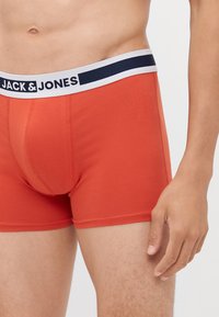 Boxer in cotone rosso con vita elastica bordata di blu, etichettata "JACK & JONES." Texture liscia e design aderente, lunghezza a metà coscia.