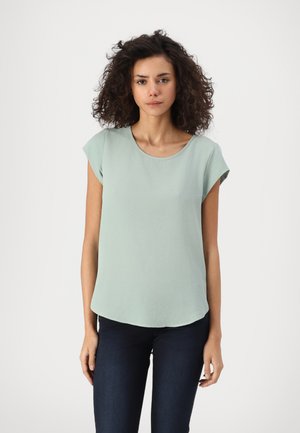 Haut vert clair à manches courtes avec un col rond, texture douce et ourlet légèrement incurvé, associé à un jean bleu foncé.