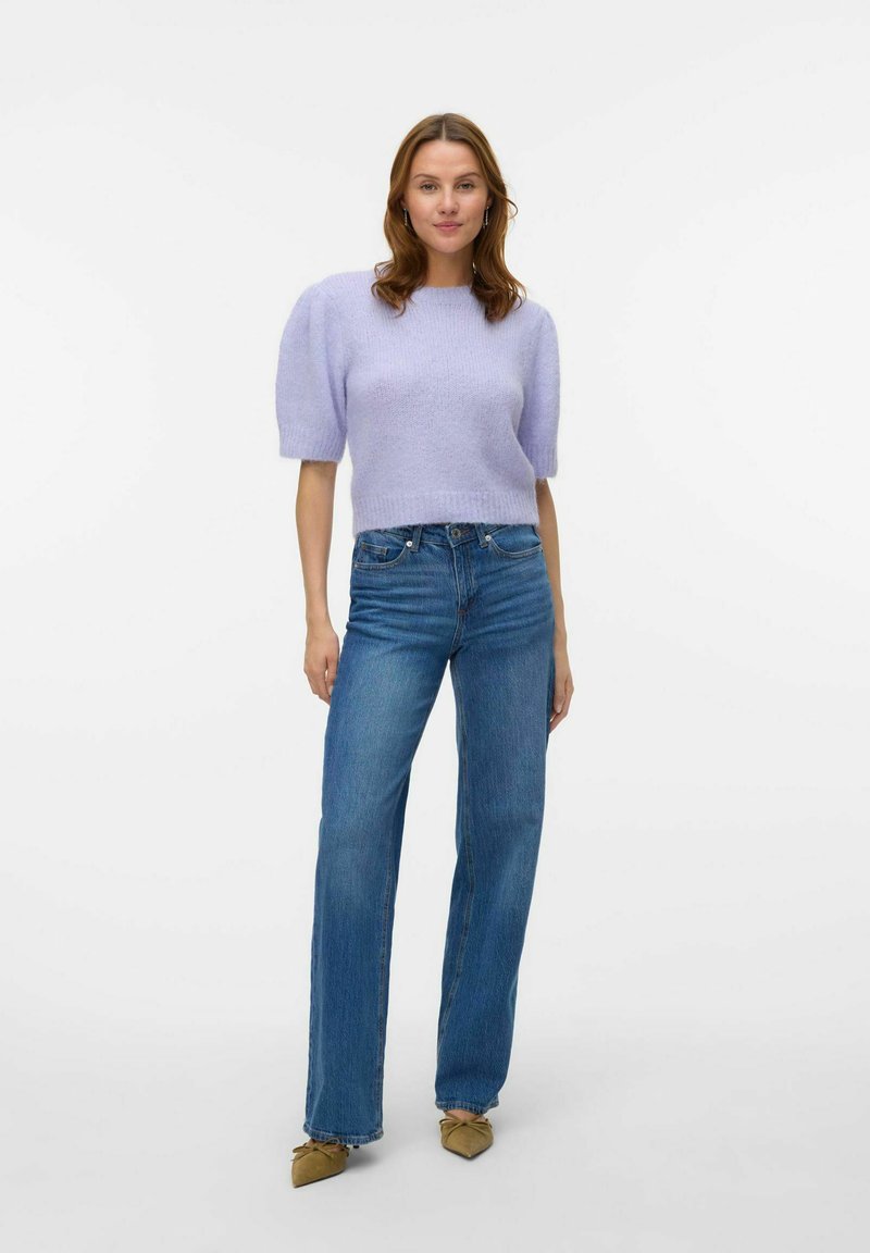 Lila pulover s kratkimi rokavi iz pletenine z teksturirano površino, kombiniran z modrimi visokotasnemi kavbojkami in rjavimi špicastimi balerinkami.