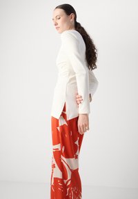 Long-sleeve cream top with side slits paired with red patterned wide-leg pants featuring floral and abstract designs.