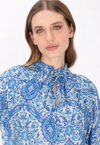 Blause mit blauem Muster, floralem und Paisley-Design, aus leichtem Stoff, mit plissiertem Ausschnitt und Bindeschluss am Kragen.