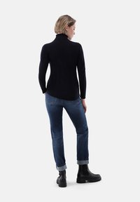 Schwarzer Rollkragenpullover kombiniert mit blauen Jeans. Das Model steht von hinten und trägt schwarze Stiefeletten mit dicker Sohle.