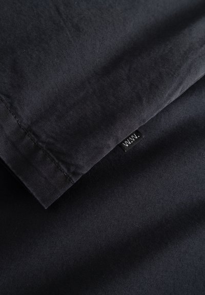 Tume riie, mis on voltitud, nähtava õmblusega ja väikese musta sildiga, millel on kiri "W.N.W.", kinnitatud ääre lähedale.