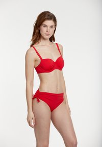 Czerwony zestaw bikini składający się z topu z formowanymi miseczkami i regulowanymi ramiączkami oraz majtek z wysokim stanem, zdobionych marszczeniami i wiązaniami po bokach.