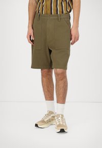 Khaki cargo shorts with a relaxed fit, featuring front pockets, a zip fly, and a smooth texture. Paired with beige sneakers and white socks.