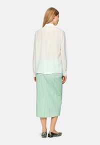 White blouse with a pleated back detail, paired with a mint green, knee-length pleated skirt and patterned flats.