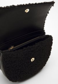 Black leather bag with a textured black wool flap, gold hardware, magnetic closure, and an interior zip pocket. Smooth lining.