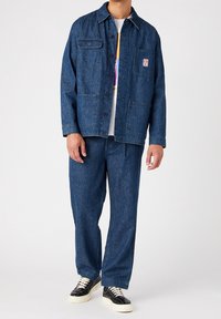 Farkkutakki kahdella etutaskulla ja nappikiinnityksellä, yhdistettynä samansävyisiin löysiin farkkuihin. Tumma sininen väri, teksturoitu kangaspinta.