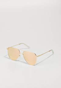 Occhiali da sole in metallo dorato con forma geometrica. Lenti riflettenti rosa e punte in plastica trasparente sulle tempie. Design slim e minimalista.