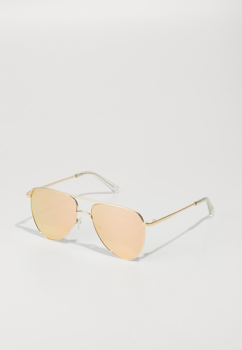 Occhiali da sole in metallo dorato con forma geometrica. Lenti riflettenti rosa e punte in plastica trasparente sulle tempie. Design slim e minimalista.