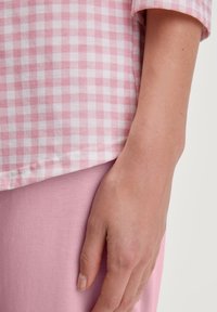 Roze en witte geblokte shirtsstof met een lichte textuur, gecombineerd met een effen roze stof eronder. Hand rustend op het kledingstuk.