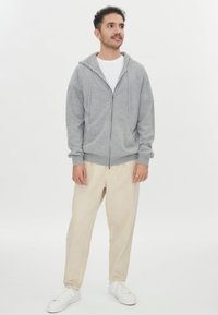 Grå zip-up hoodie med dragsko i huvan, framfickor och ribbad mudd. Kombinerad med beige byxor och vita sneakers.