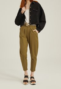 Chaqueta de mezclilla negra recortada con cierre de botón, top blanco, pantalones de cintura alta verde oliva y sandalias negras con suelas blancas.