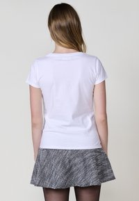 Camiseta blanca de manga corta con escote redondeado, combinada con una falda plisada gris y texturizada. La vista trasera muestra un diseño y ajuste sencillos.
