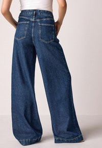 Weite blaue Denim-Jeans mit hoher Taille, ausgestattet mit Gesäßtaschen und kontrastierenden Nähten entlang der Säume.