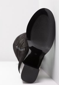 Bottine en suède noir avec une semelle en cuir lisse, présentant un petit talon carré et des détails texturés sur la semelle pour une meilleure adhérence. Taille 37.