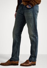 Modré džíny z denimu s úzkým střihem, které mají jemné vyblednutí a klasický pětikapsový design. Nosit s hnědými koženými mokasíny.