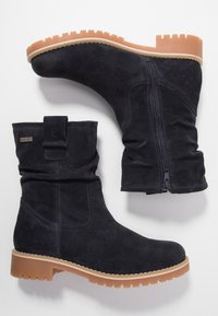 Botines de ante negro con cremallera lateral. Presentan una suela de goma resistente y un cuello suave y doblado con un detalle de correa.