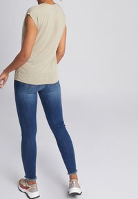 Beige kortärmad topp, åtsittande denimjeans och flerfärgade sportskor. Jeansarna har en klassisk femficksdesign och detaljer med fransar i fållen.