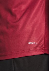 Punainen urheilu paita, joka on valmistettu hengittävästä materiaalista ja jossa on teksturoitu kangas. Sisältää valkoisen "DRYCELL"-tarran helman lähellä.