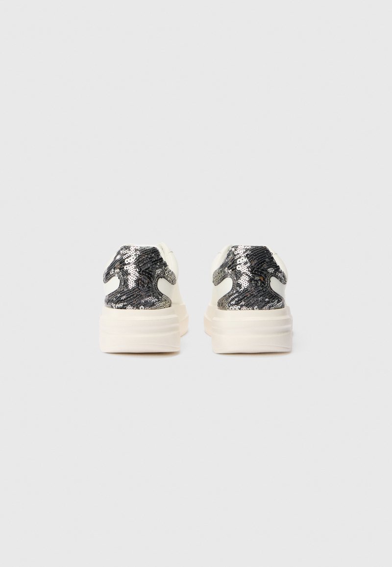 Zapatillas deportivas blancas de plataforma vistas desde la parte trasera, con paneles de tacón de lentejuelas negras y plateadas.