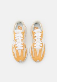 Baskets légères avec une tige en mesh blanc, des accents en daim jaune, des lacets blancs plats et une semelle rembourrée, présentant un design minimaliste.