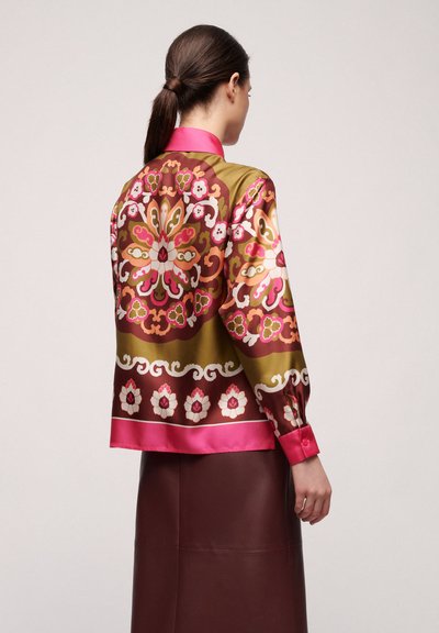 Blouse en soie avec un motif floral dans des tons de rose, vert et marron. Fini satiné, manches longues, et col et poignets roses.