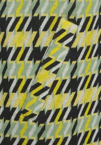 Tessuto con motivo a zigzag nei colori verde, giallo, nero e bianco, con un piccolo dettaglio di tasca visibile sulla superficie.
