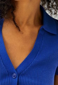 Blaues geripptes Strickjacke mit tiefem V-Ausschnitt, kurzen Ärmeln und einem einzigen Knopfverschluss. Weiche Textur mit sichtbarem Rippenmuster.
