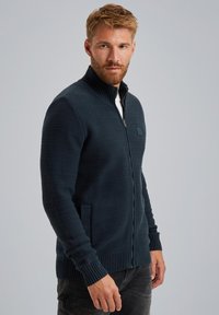 Donkerblauwe gebreide zip-up trui met een hoge kraag, voorzien van geribde manchetten en onderrand, en zijzakken. Gelaagde stof met een modern ontwerp.
