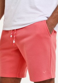 Pantaloni corti color corallo realizzati in misto cotone, con vita regolabile con cordoncino e accenti rossi e bianchi e tasche laterali.
