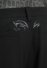 Μαύρο παντελόνι με απαλό ύφασμα, ελαστική μέση και διακριτικά γυαλιστερά φυλετικά σχέδια στις περιοχές των πίσω τσεπών.