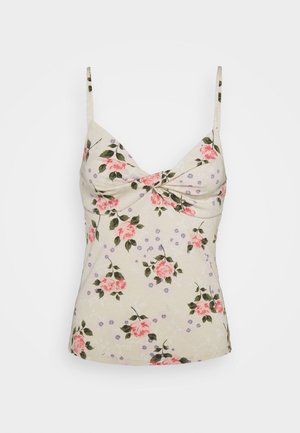 Camisole florale à fines bretelles avec un fond crème, des roses roses et des accents violets. Texture douce et design avant torsadé.