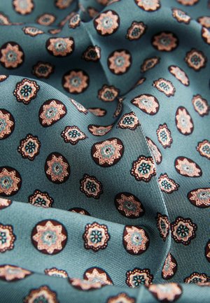 Musterstoff mit einem türkisen Hintergrund und kleinen Blumenmotiven in Rosa- und Blautönen, akzentuiert von dunklen kreisförmigen Umrandungen.