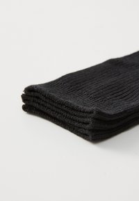 Sorte ribbede sokker stablet, lavet af et blødt tekstilmateriale med en glat overflade. Den øverste sok har en pæn kant.