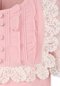 Roze top met gestructureerde ruches en een geschulpte kantafwerking aan de zoom. Glad materiaal met knoopdetails aan de voorkant.