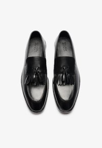 Zwarte leren loafers met een glad oppervlak, kwastaccenten, ronde neus en een platte zool. Merk zichtbaar op de binnenzool.