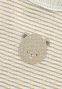 Pruhovaná tkanina ve světlé béžové a krémové barvě má grafiku medvědí tváře v tlumené béžové barvě, s jemnou texturou a zaoblenými tvary.