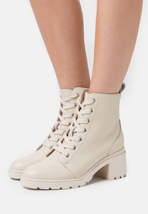 Botines de cuero texturizado en beige con cordones presentan un tacón grueso y una suela resistente, con herrajes de plata y una lengüeta en la parte trasera.