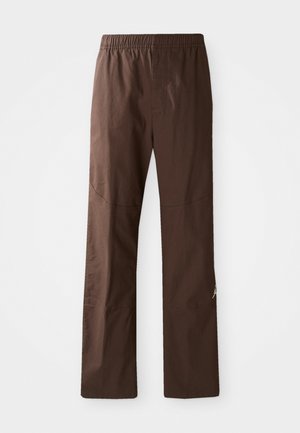 Bruine broek met rechte pijpen, voorzien van een elastische tailleband en subtiele naden, gepresenteerd tegen een witte achtergrond.